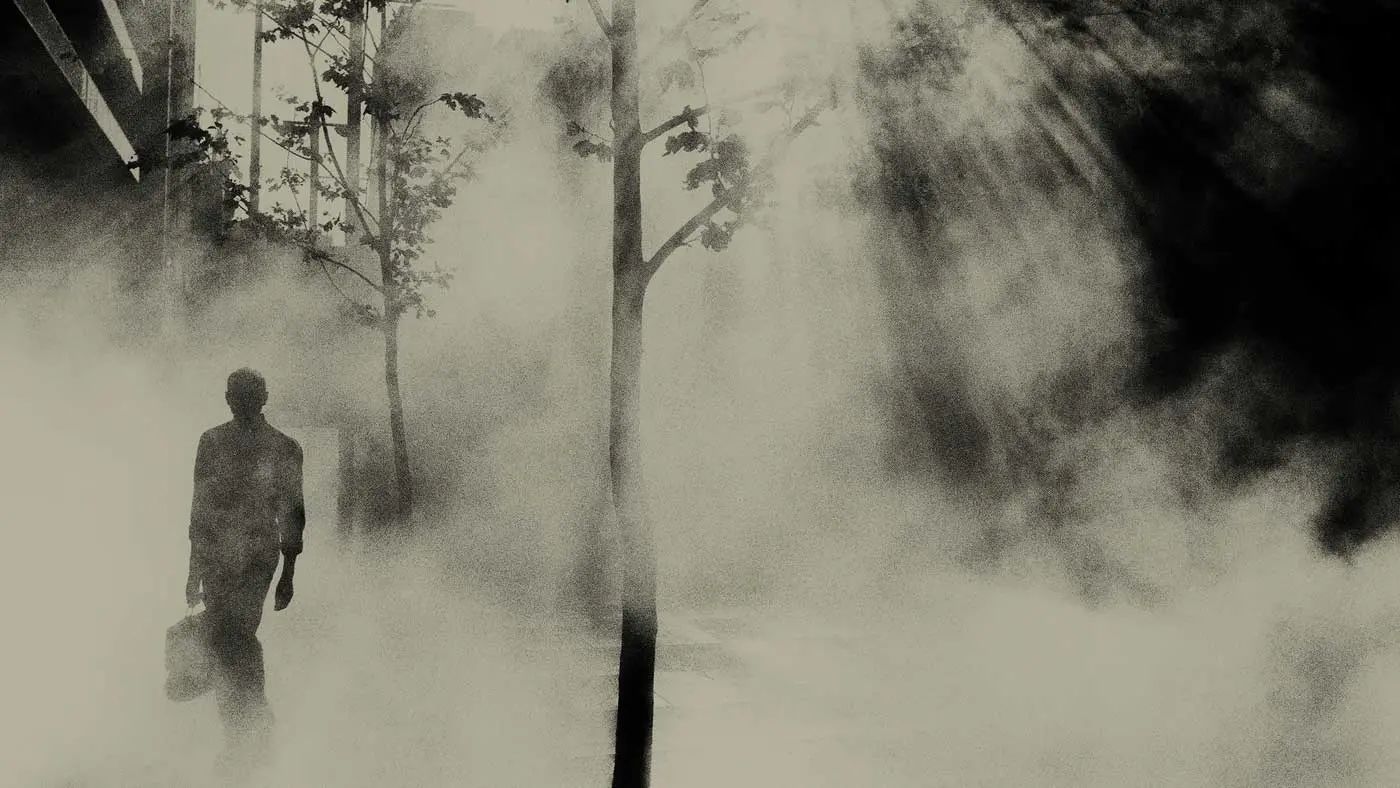 Black and white image of a person walking through a misty forest.